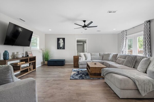 A modern living room with a flat-screen TV, a ceiling fan, and a large sectional sofa.