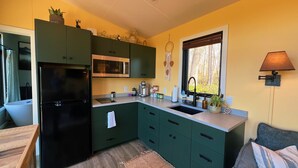 Una cucina con mobili verdi, un frigorifero nero, un forno a microonde e una finestra con vista sugli alberi.