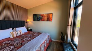 Et hotelværelse med seng, et natbord, en lampe, et vindue og et billede på væggen.