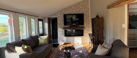 Una sala de estar con chimenea, ventilador de techo y televisor grande montado en la pared.