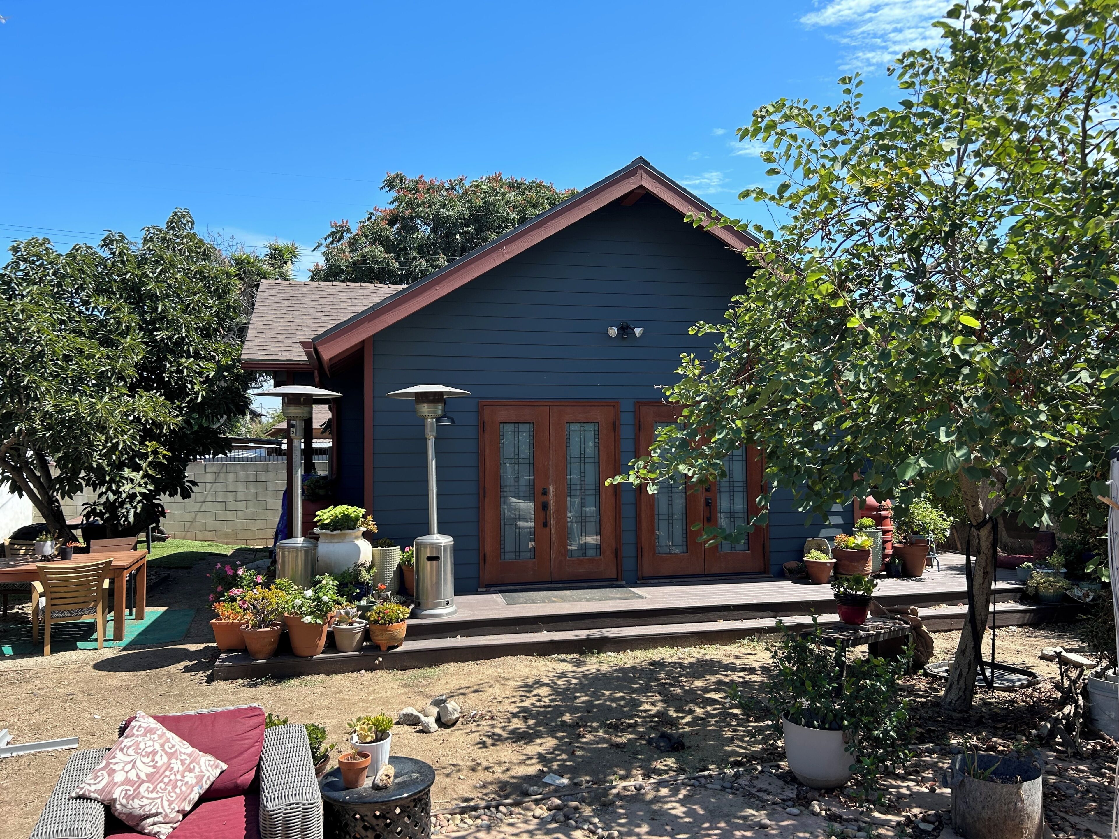 A small building with a dark exterior, a front door, and a small porch area with outdoor seating and potted plants.