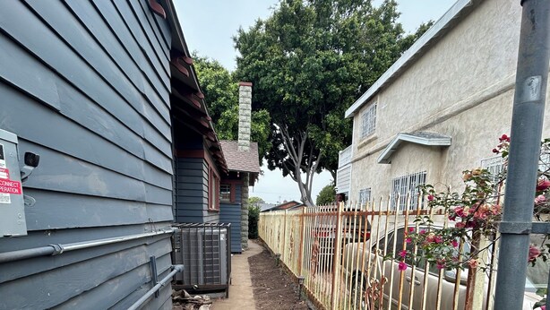 Um caminho estreito ladeado por edifícios, uma cerca de metal e uma árvore.