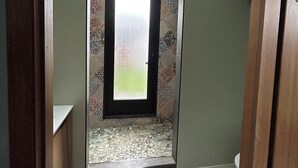 Um corredor estreito com um claraboia, parede estampada e porta que dá para um quarto com chão ladrilhado.