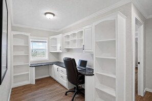 A compact kitchen with built-in white cabinets, a dark countertop, and a single chair.