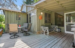 Eine Holzterrasse mit Gartenmöbeln, eine überdachte Terrasse und ein Gebäude mit grüner Fassade.