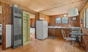 A compact kitchen with a refrigerator, stove, and a small dining table with a chair. - Camp Intermediate - Two Lakefront Pet Friendly Cabins! (Central Lake)