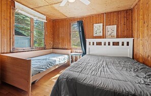 Ein blockhaushaltiger Raum mit Etagenbett und Einzelbett, Holzvertäfelung und Deckenventilator.