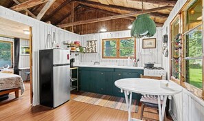 Ein rustikales Blockhaus-Interieur mit Küche, Essbereich und einem großen Fenster mit Blick ins Freie.