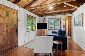 Ein rustikales Blockhaus-Interieur mit Holzbalkendecke, einem Fernseher, einer Couch und einem Sessel.