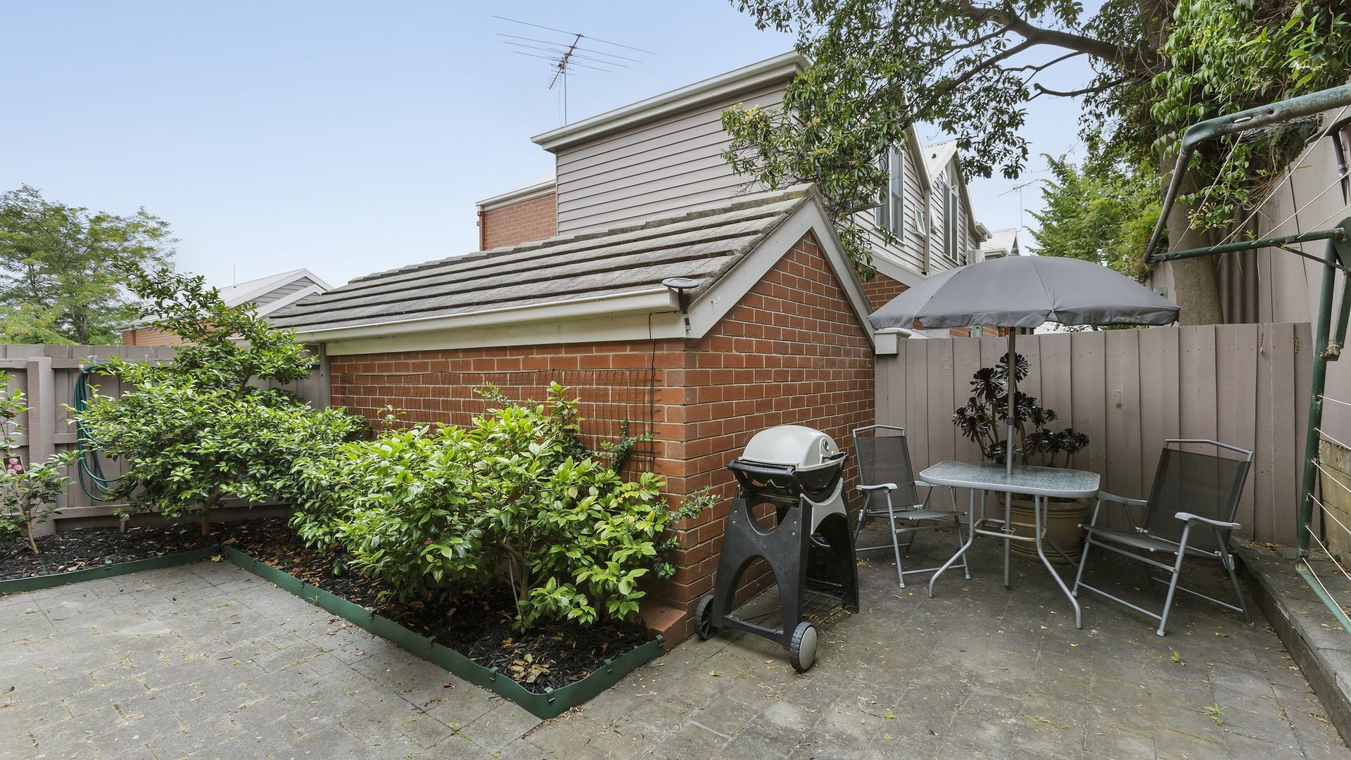 A backyard with a barbecue grill, a table with chairs, and a wooden fence.