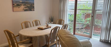 Comedor con una mesa dispuesta para seis personas, rodeada de sillas, un cuadro en la pared y vistas a través de un ventanal.