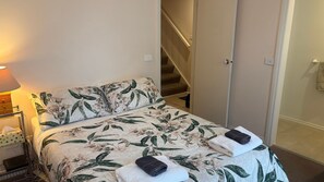 A bed with floral bedding, a bedside lamp, a nightstand, and a folded towel. - Osprey 1 - Queenscliff (QUEENSCLIFF)