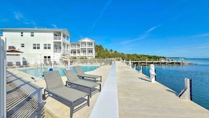 A poolside area with lounge chairs, a pool, and a pier extending into the water.