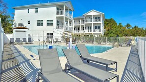 A pool area with lounge chairs and a building with multiple balconies.