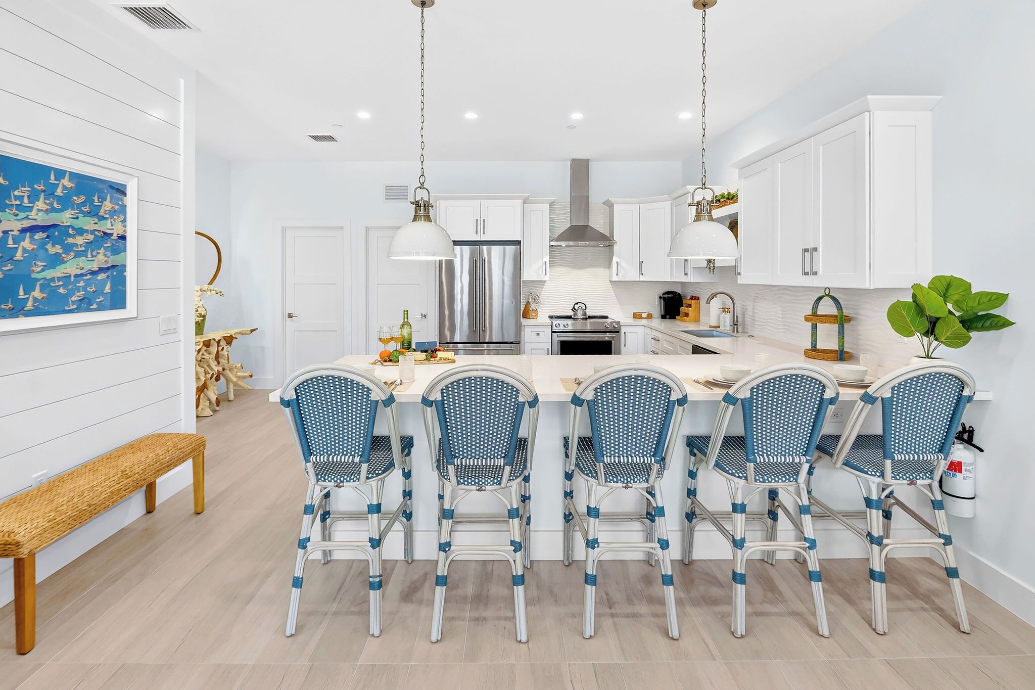 Une cuisine moderne avec des meubles blancs, un îlot central doté de chaises et un luminaire suspendu.