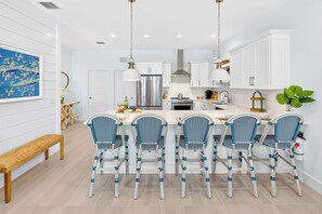 A modern kitchen with white cabinetry, a central island with chairs, and a hanging light fixture.