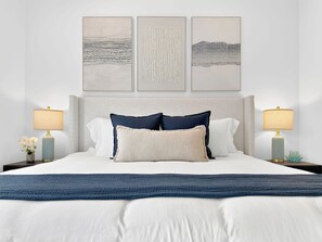 Un lit bien fait, avec une couvre-lit bleue, deux oreillers et une tête de lit. Trois œuvres d’art encadrées sont accrochées au mur au-dessus du lit.