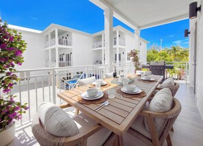 A covered outdoor dining area with a wooden table set for four, surrounded by wicker chairs with cushions.