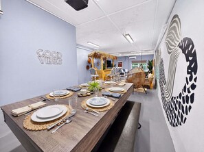 A dining area with a long wooden table set for a meal, a wall with a 'GOOD VIBES' sign, and a large abstract wall art piece.