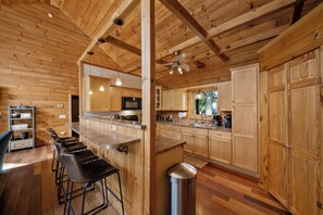 A wooden interior with a kitchen area featuring bar stools, a ceiling fan, and wooden cabinets. - Spacious Mountain Getaway Minutes from Boone (Boone)