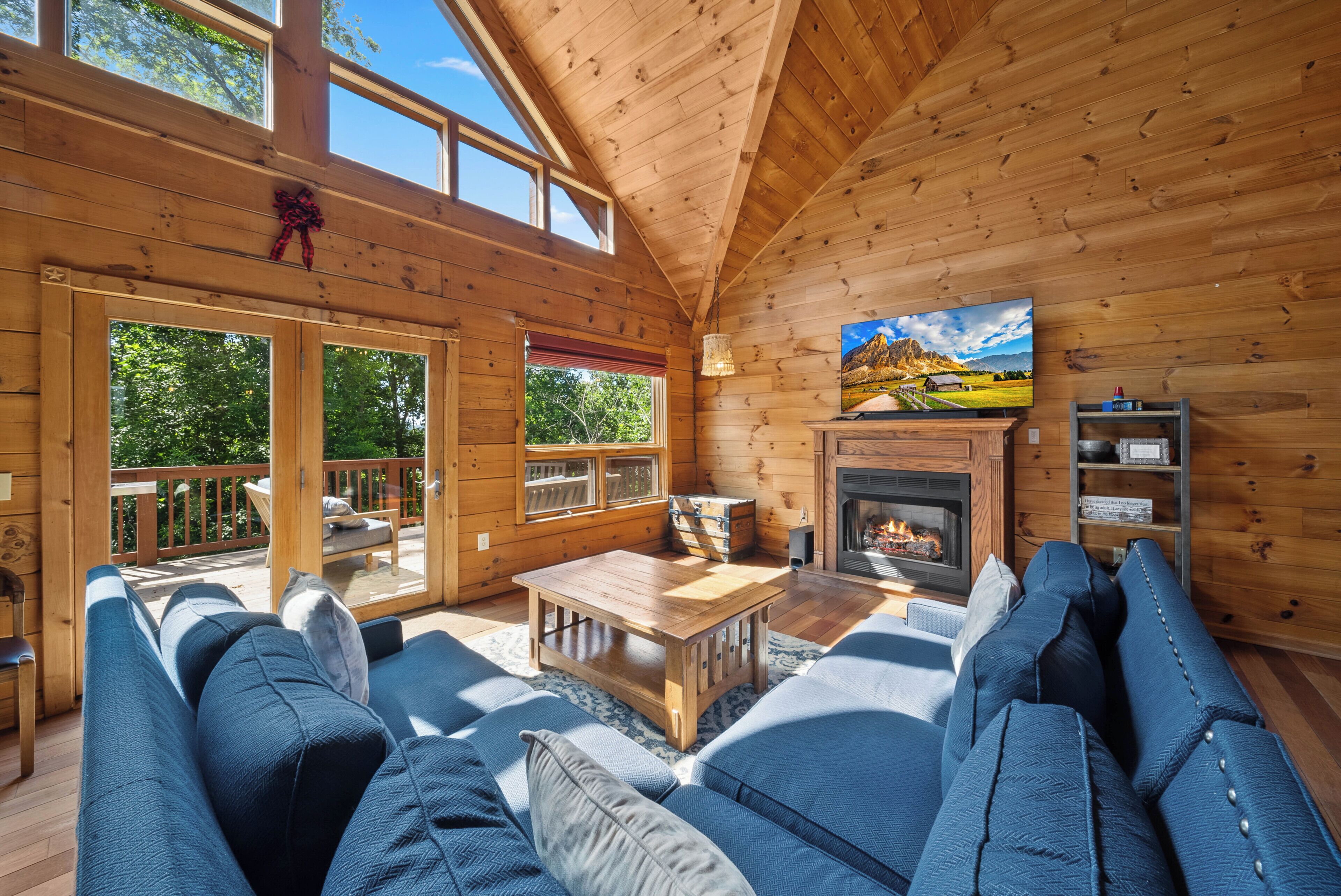 A cozy log cabin interior with a fireplace, wooden furniture, and large windows.