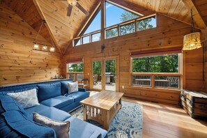 A wooden cabin interior with a sofa, table, and large windows. - Spacious Mountain Getaway Minutes from Boone (Boone)