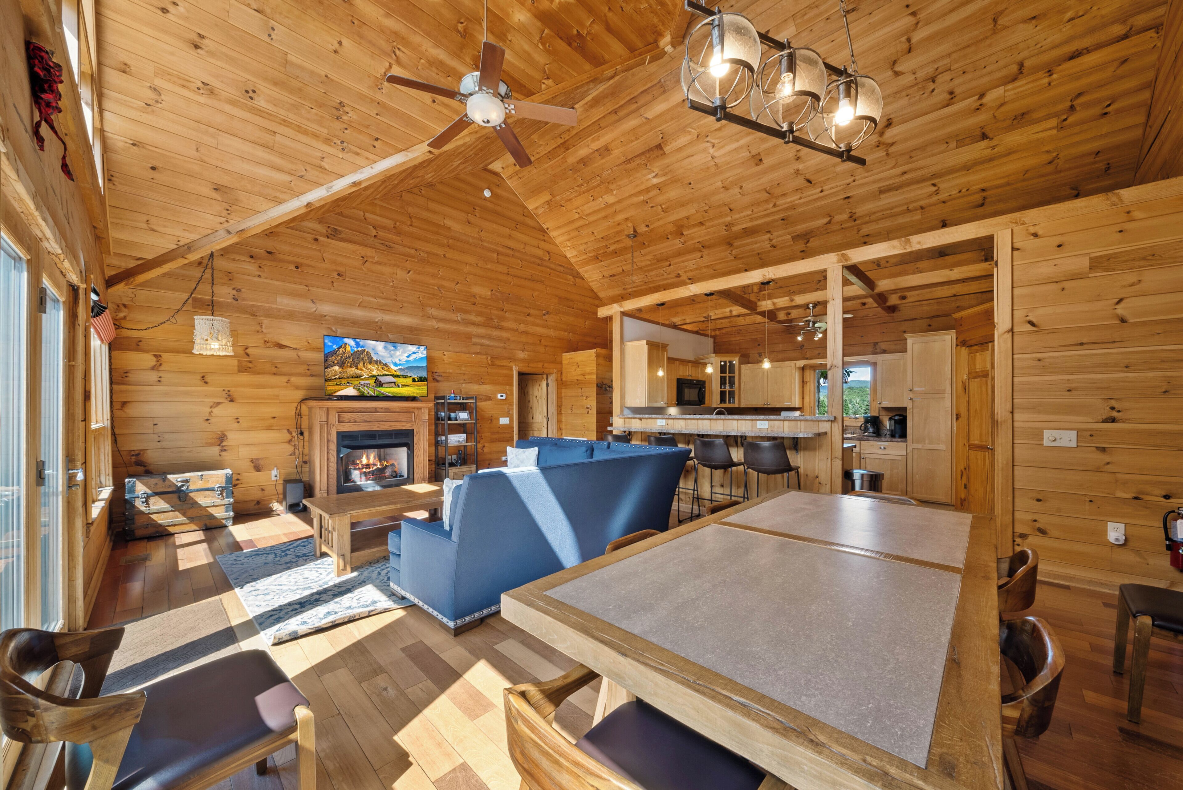 A cozy log cabin interior with a fireplace, a dining area, and a kitchen.