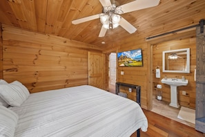 A wooden room with a bed, a ceiling fan, a TV, and a bathroom with a sink and mirror. - Spacious Mountain Getaway Minutes from Boone (Boone)