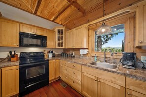 A kitchen with wooden cabinets, a black microwave, a stove, a sink, and a coffee maker. - Spacious Mountain Getaway Minutes from Boone (Boone)