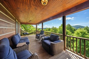 A covered outdoor deck with wicker furniture and a hammock, overlooking a forested landscape. - Mountain Retreat with Long-Range Views Near Boone (Boone)