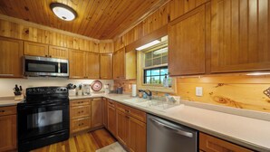 A kitchen with wooden cabinets, a microwave, stove, dishwasher, and a window with a view. - Mountain Retreat with Long-Range Views Near Boone (Boone)