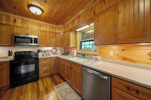 A kitchen with wooden cabinets, a microwave, stove, dishwasher, and a window with a view. - Mountain Retreat with Long-Range Views Near Boone (Boone)