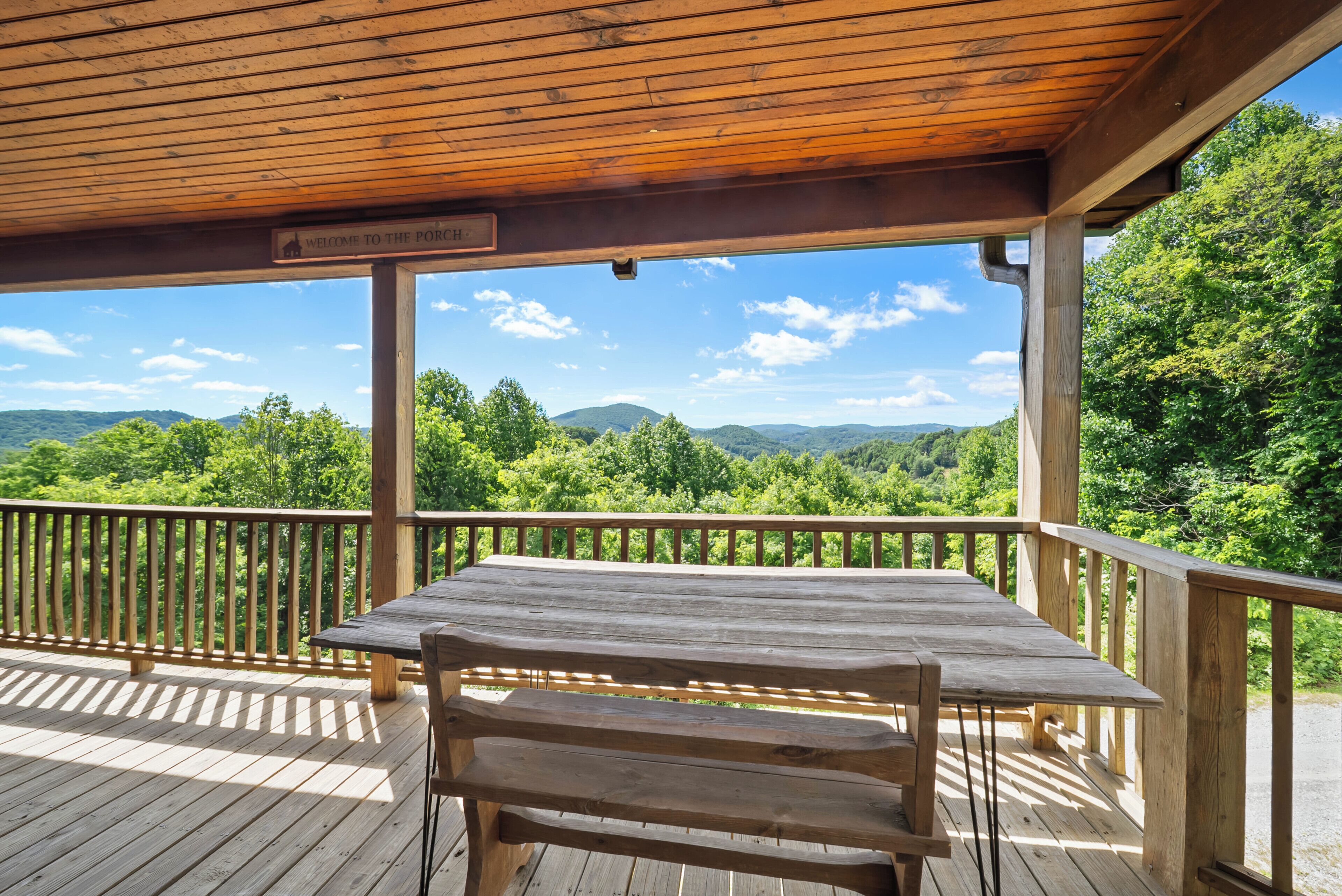 A wooden deck with a table and bench, overlooking a forested landscape with hills.