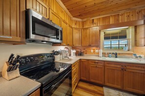 A kitchen with wooden cabinets, a stainless steel microwave, a stove, and a window with a view. - Mountain Retreat with Long-Range Views Near Boone (Boone)
