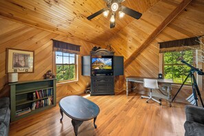 A cozy room with wooden walls and ceiling, a television, a desk with a chair, a bookshelf, and a window with a view of greenery. - Mountain Retreat with Long-Range Views Near Boone (Boone)