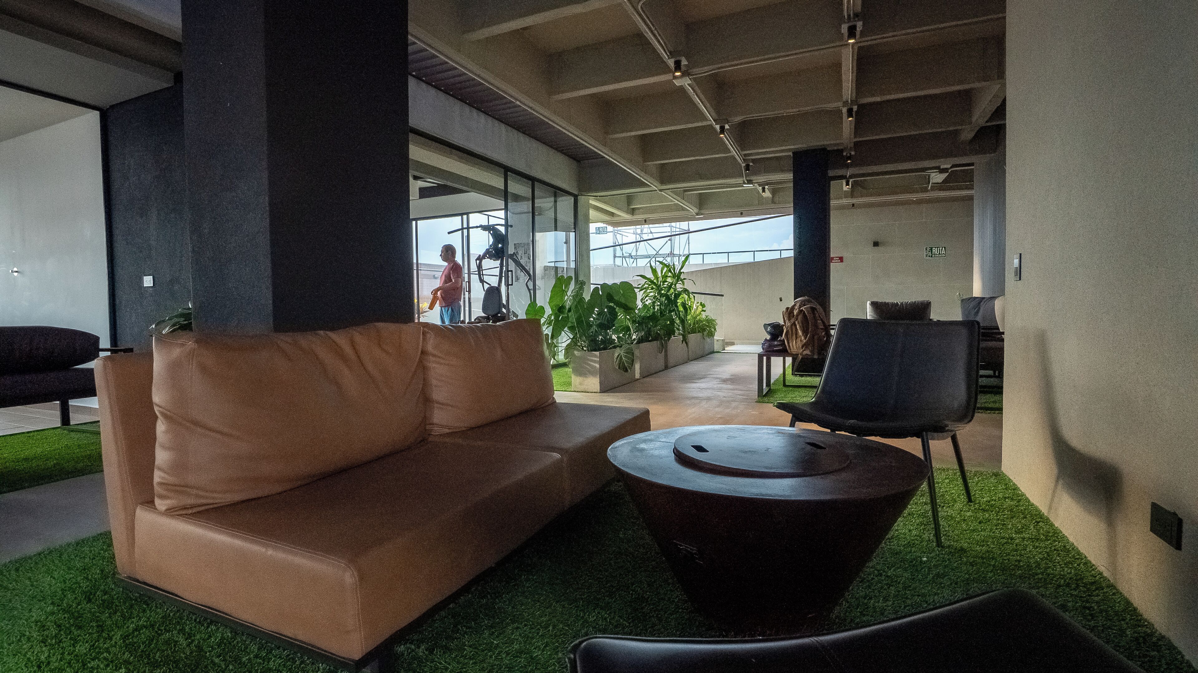 A modern lounge area with a sofa, a round table, and chairs, featuring a view of the sky through large windows.