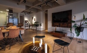 Un intérieur moderne comprenant un coin repas avec une table et des chaises en bois, un coin cuisine avec une cuisinière et des placards, et un grand téléviseur à écran plat fixé au mur.