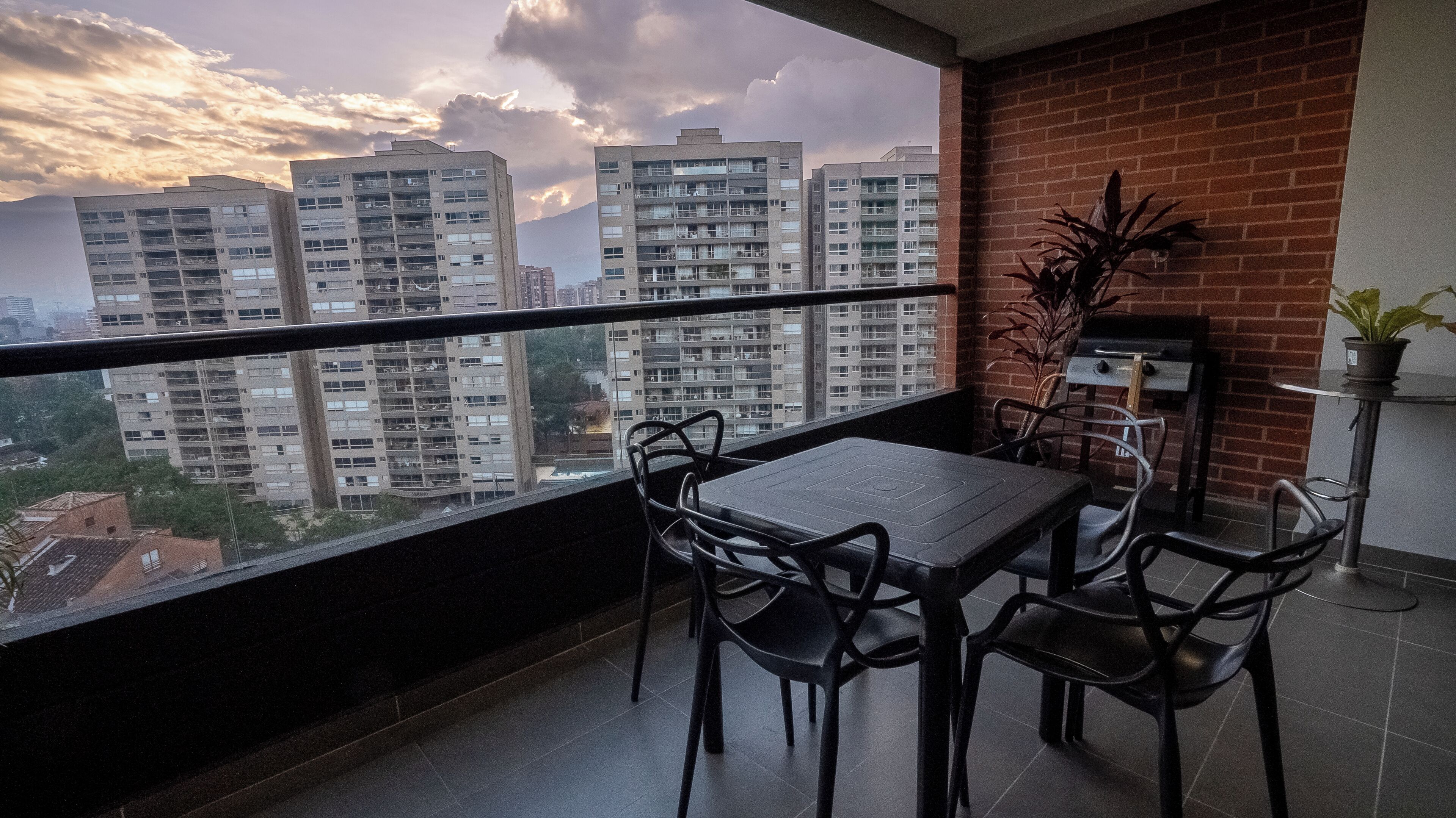 Un balcon avec une table et des chaises, un barbecue et une plante en pot.