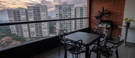 Un balcón con mesa y sillas, una parrilla y una planta en maceta.