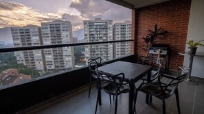 Een balkon met een tafel, stoelen, een barbecue en een bloempot.
