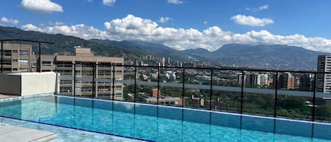 A rooftop infinity pool with a clear view of a cityscape and mountains in the background.