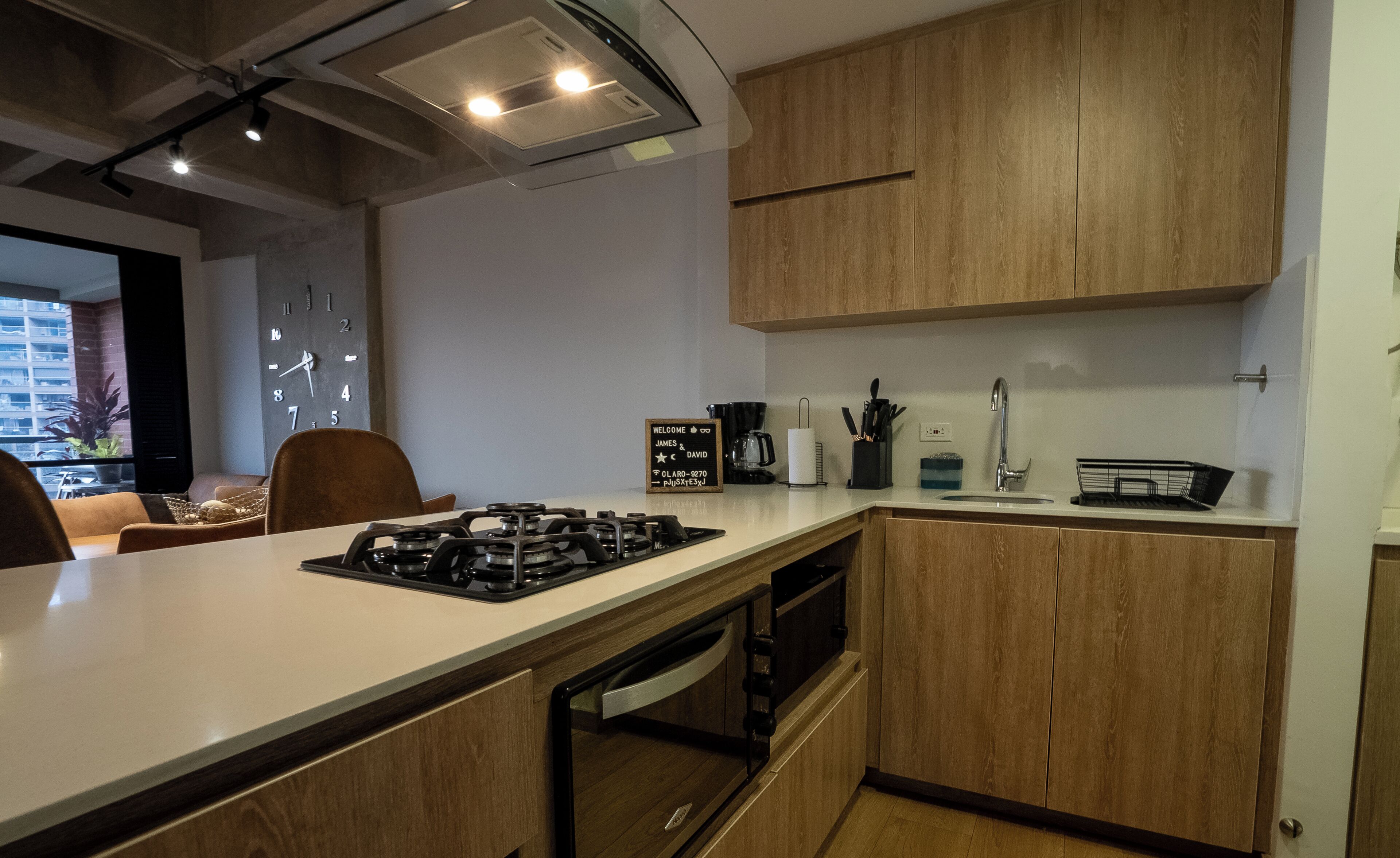 Una cocina moderna con armarios de madera, estufa a gas, cafetera y pileta.