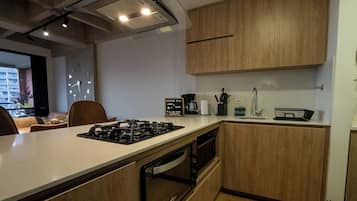 Una cocina moderna con armarios de madera, estufa a gas, cafetera y pileta.