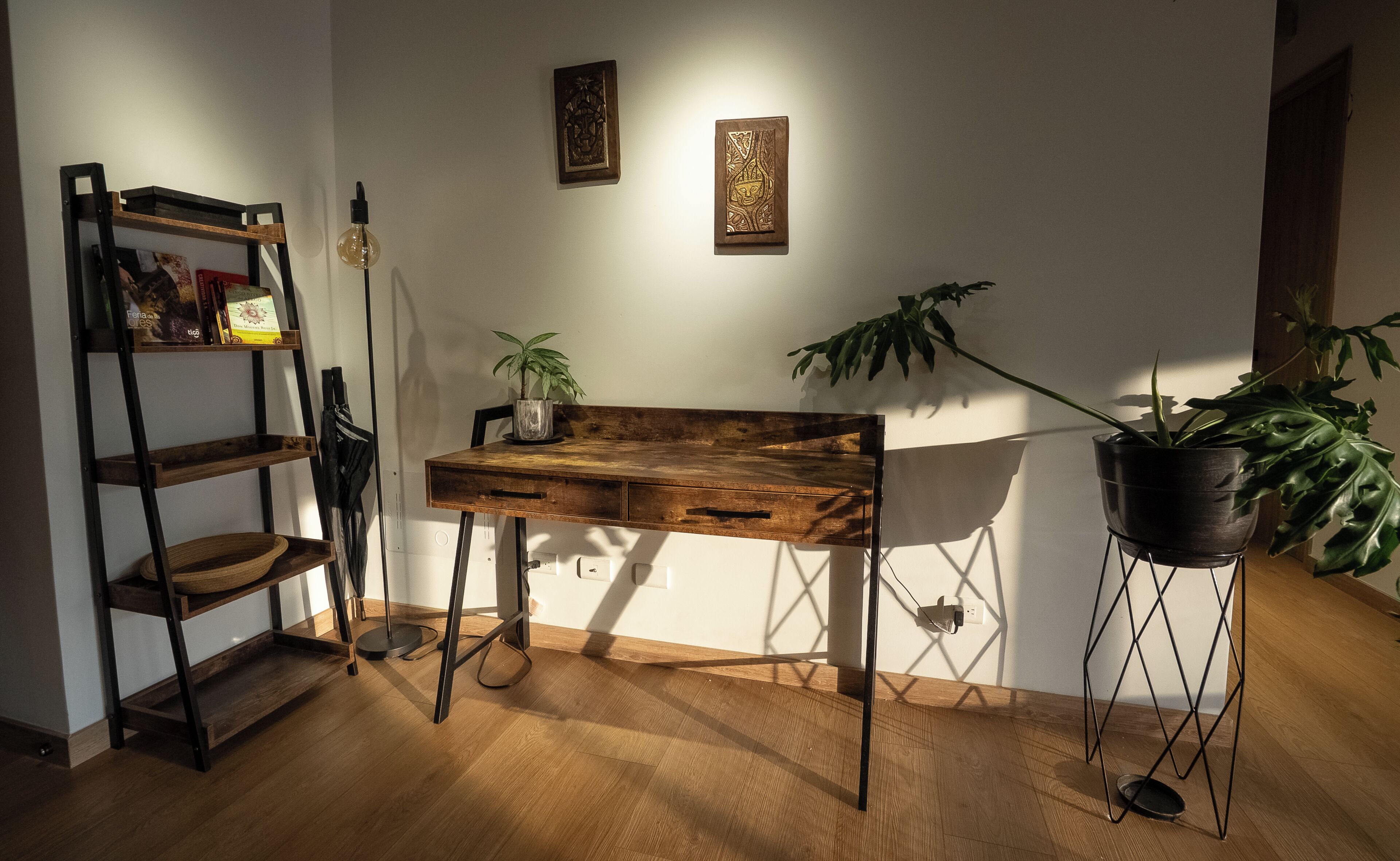 Une pièce avec un bureau en bois, une plante, une échelle et des œuvres d’art accrochées au mur.