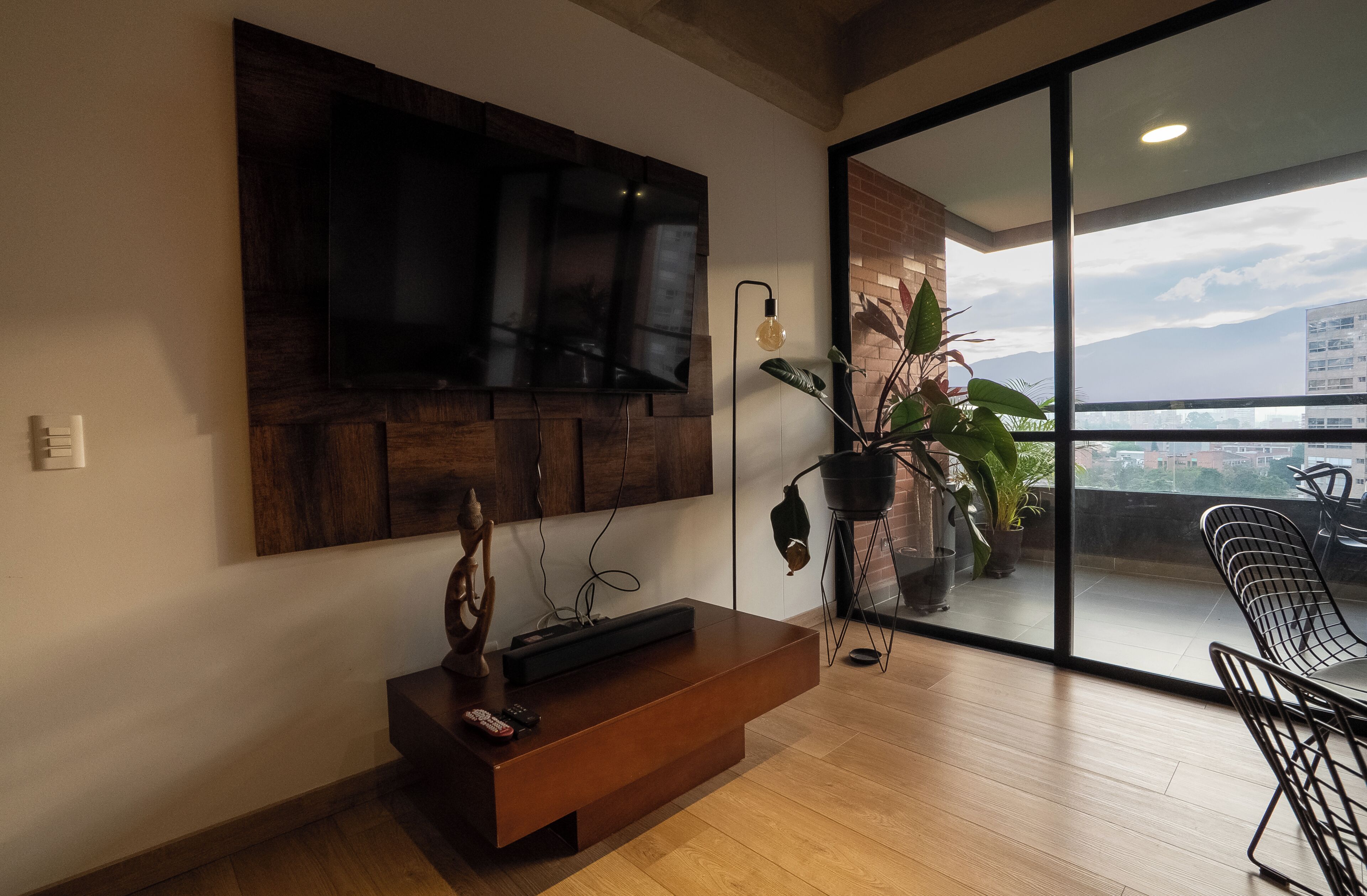 A modern living room with a flat-screen TV mounted on the wall, a wooden console table with a remote control, and a potted plant.