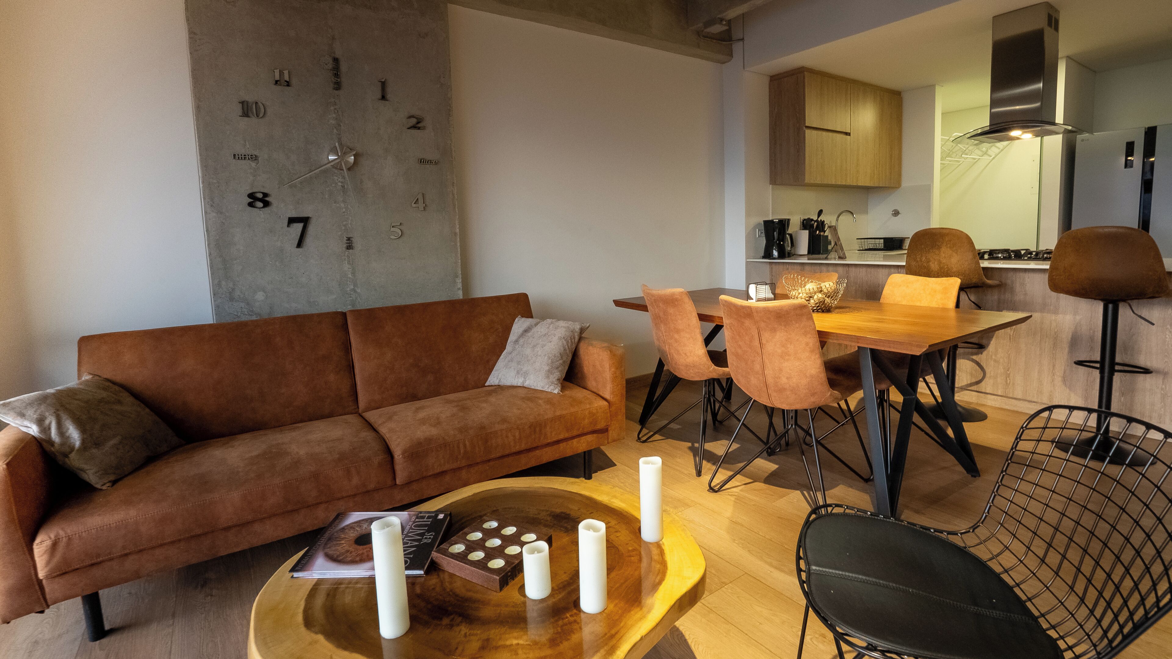 Una sala de estar moderna con un sofá marrón, una mesa de centro de madera y un comedor con mesa y sillas de madera.
