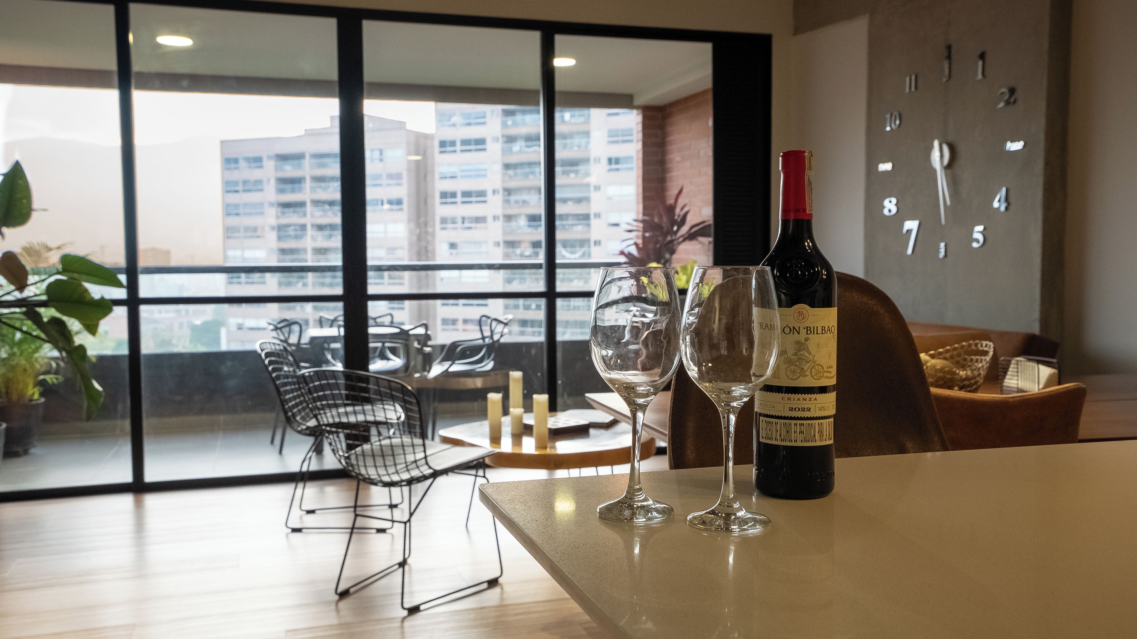Una habitación moderna con comedor, una botella de vino y un reloj en la pared.