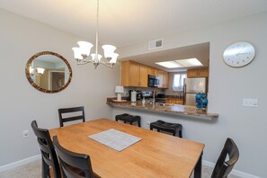 A modern kitchen with wooden cabinets, a central island, and a dining area with a wooden table and chairs. - Ocean Village Club G11, Ground Floor 2/2 Condo (St. Augustine)