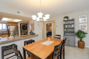 A modern kitchen with a central island, stainless steel appliances, and a dining area with a wooden table and chairs. - Ocean Village Club G11, Ground Floor 2/2 Condo (St. Augustine)