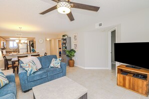 A living room with a blue sofa, a coffee table, a TV on a wooden stand, and a ceiling fan. - Ocean Village Club G11, Ground Floor 2/2 Condo (St. Augustine)